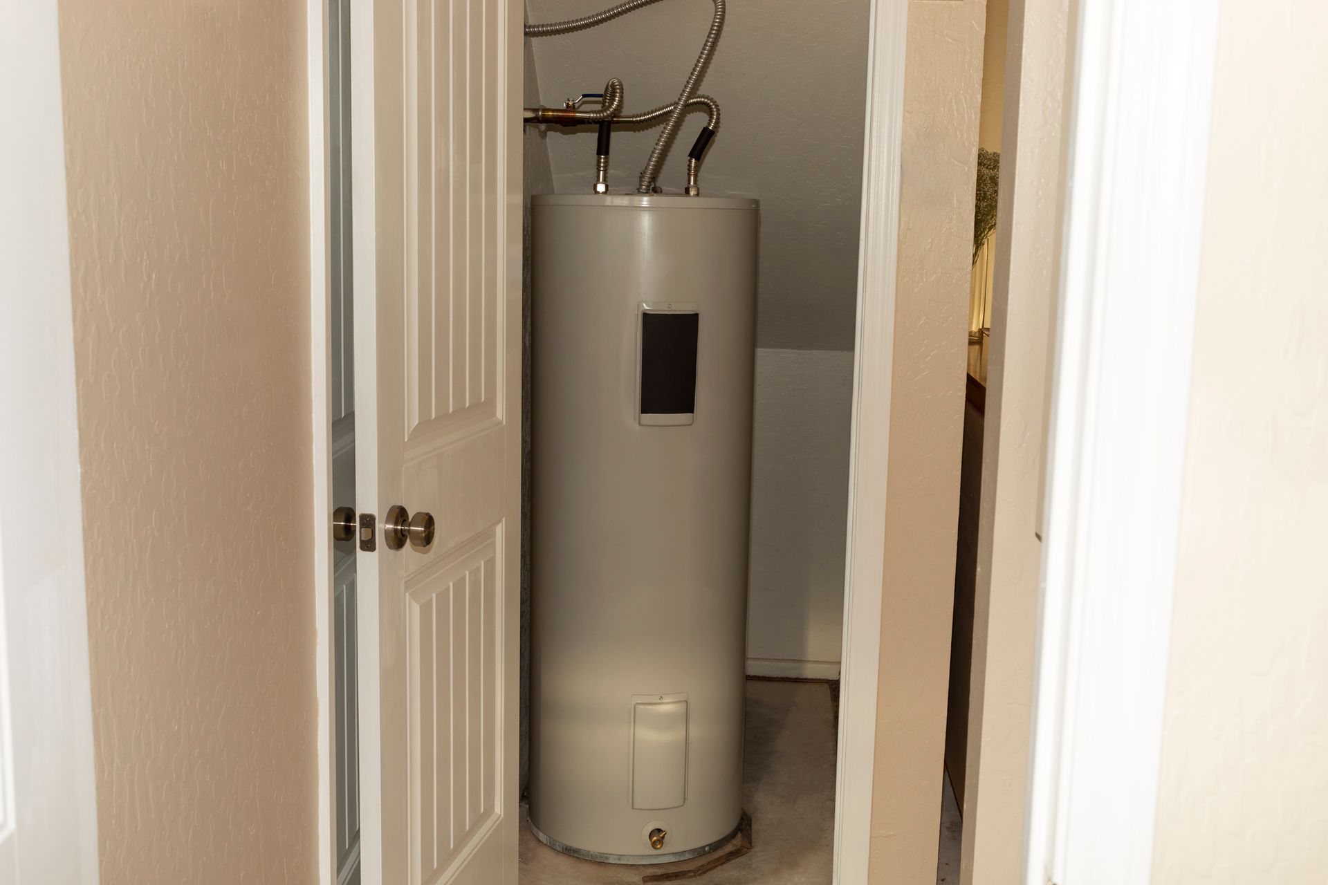 Water heater in a narrow closet with partially open white doors.