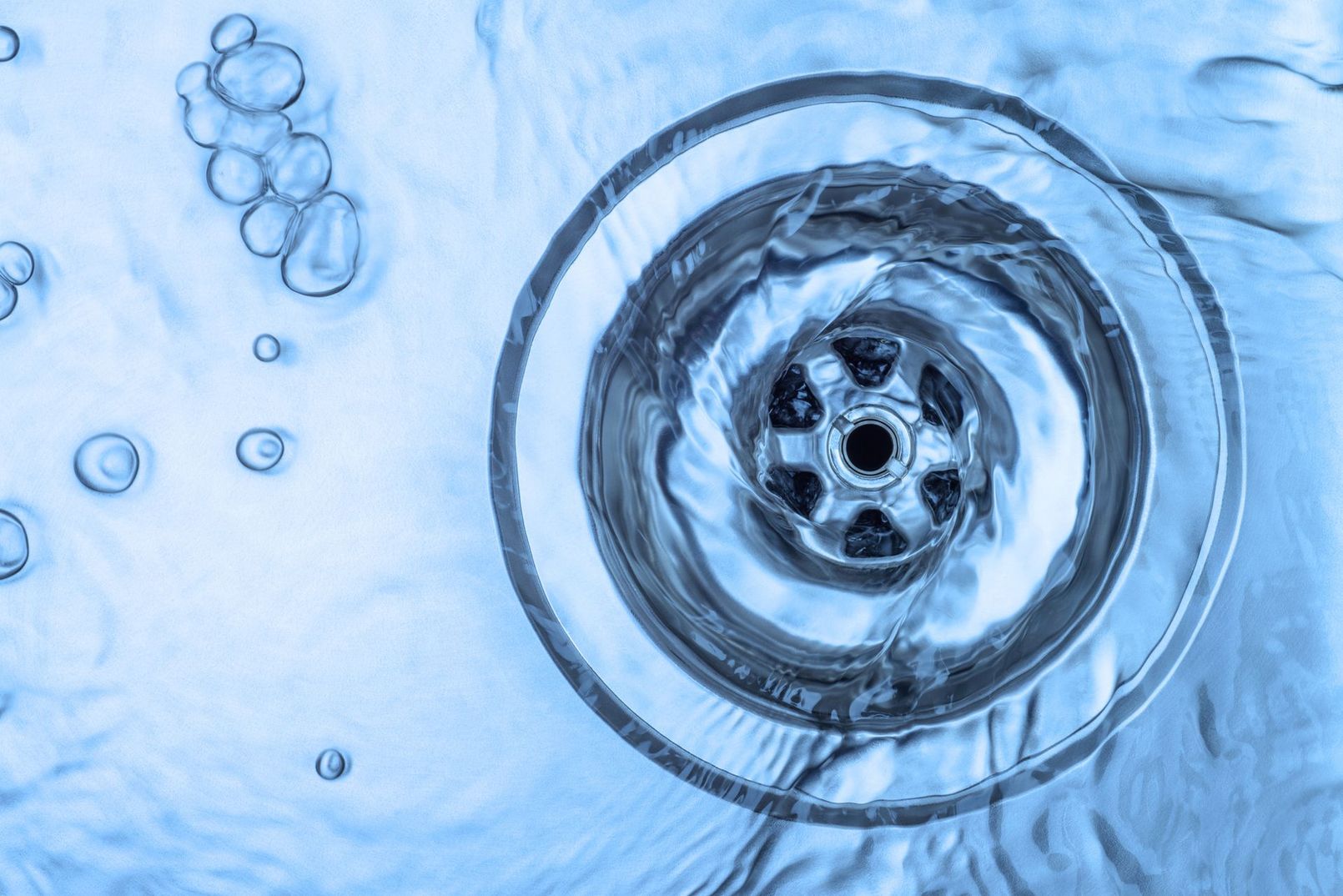 Top-down view of a metal drain with swirling water and bubbles in a blue-tinted sink
