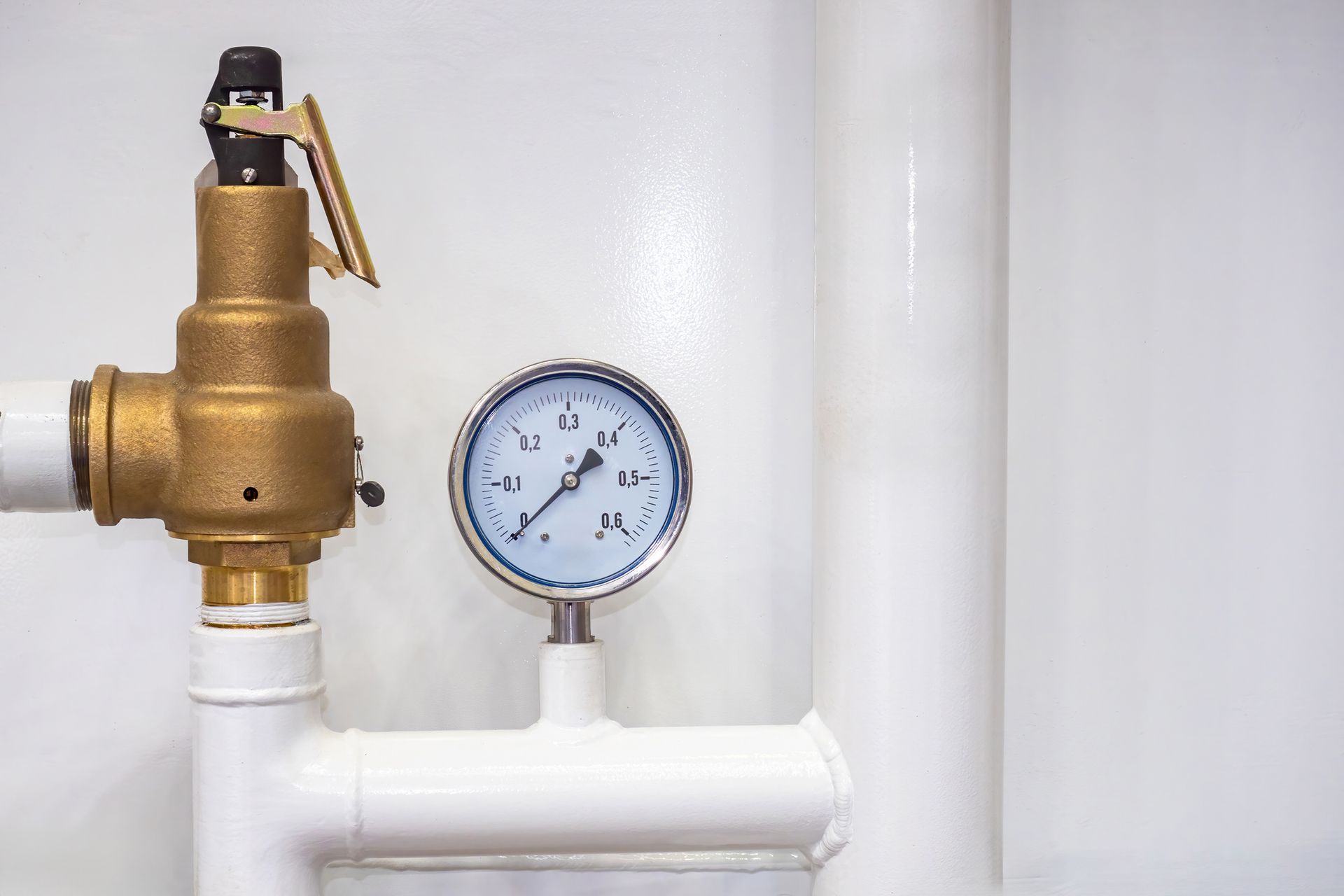 Brass pressure relief valve and round gauge on white pipes against a white wall