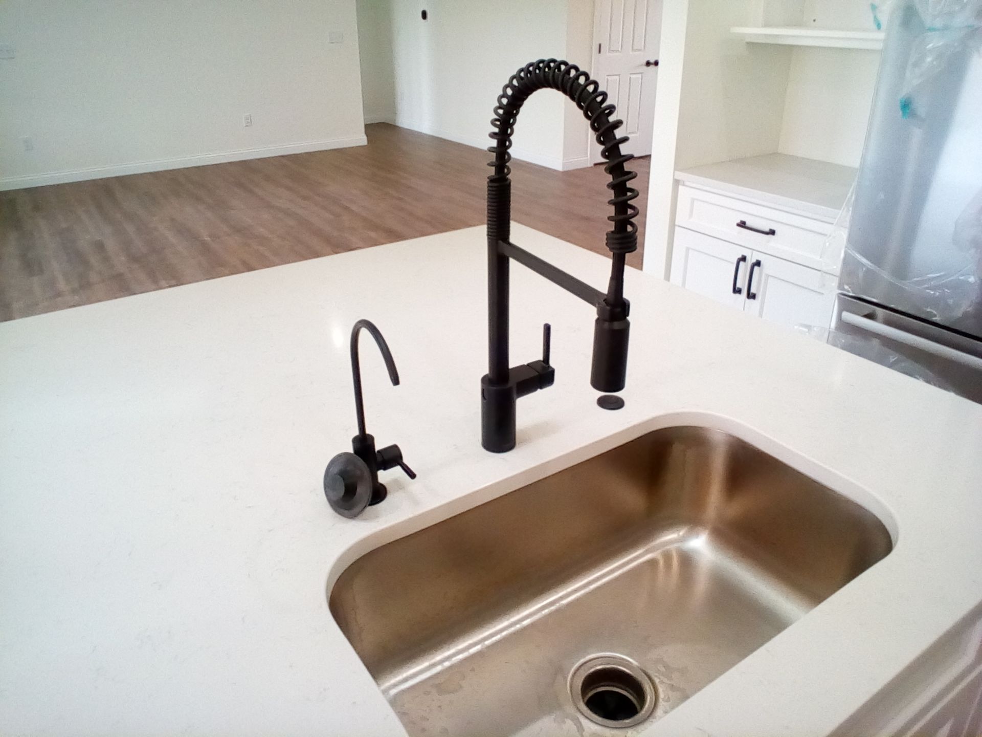 Modern kitchen with white countertop, stainless sink, and black spring faucet; a small black fixture sits nearby