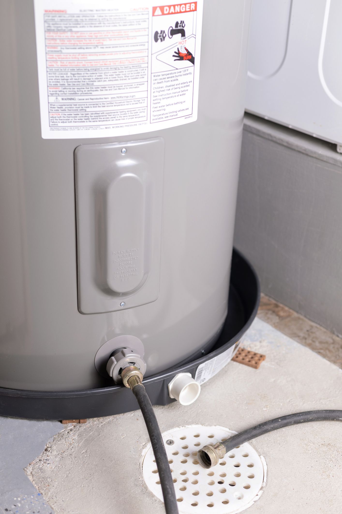 Water heater with attached hose near a floor drain and tray in a utility area
