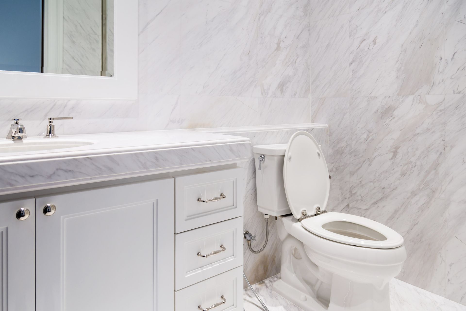 White bathroom vanity with marble countertop, mirror, and toilet against marble-patterned wall