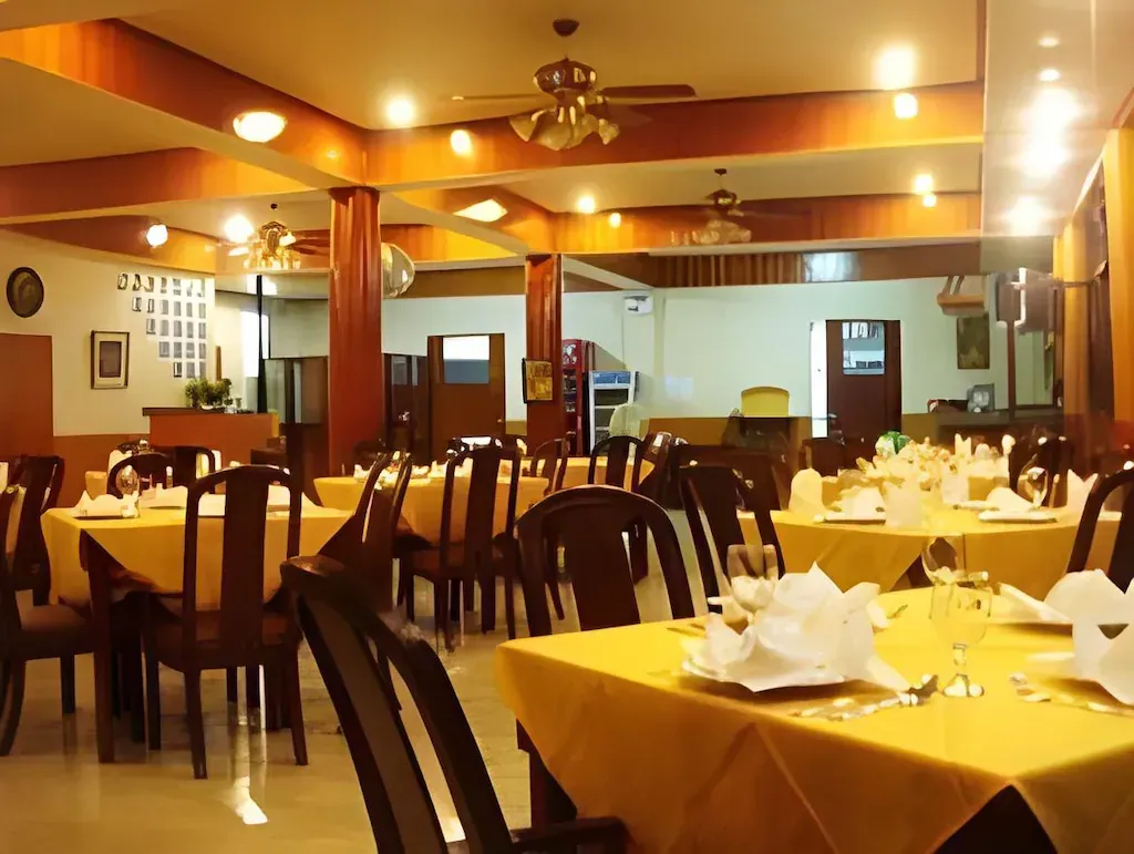 Warmly lit restaurant dining room with set tables, dark chairs, and yellow tablecloths