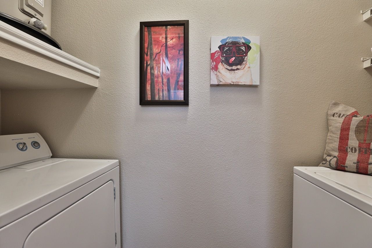 Laundry room with a washer and dryer and two framed pictures on a beige textured wall.