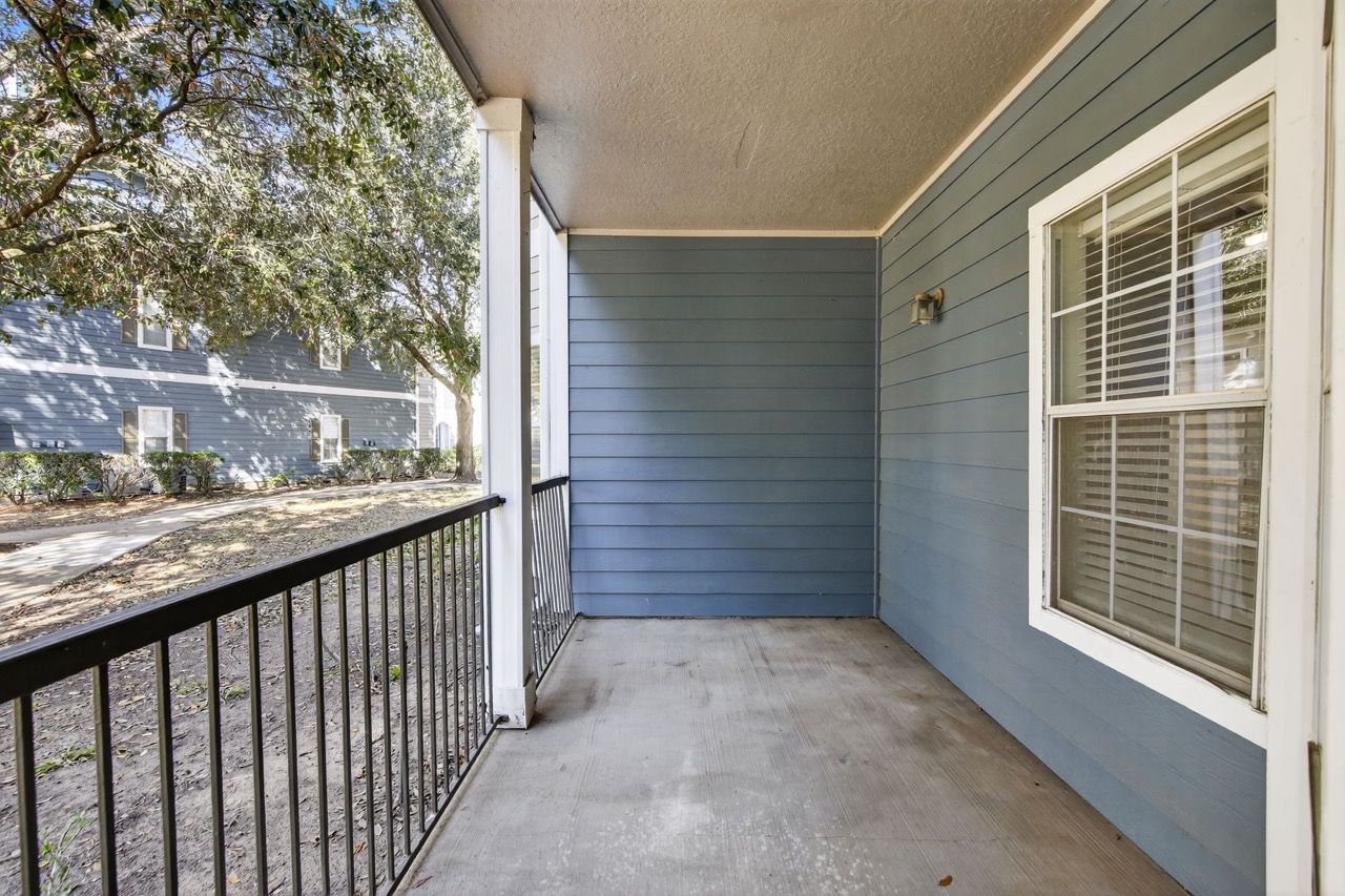 Covered apartment balcony with blue siding, railing, and a window.