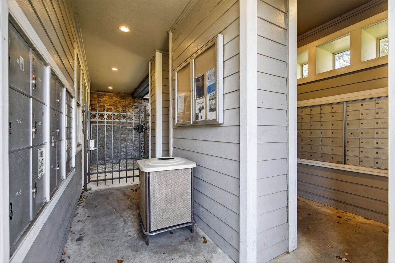Covered exterior corridor with metal mailboxes along the wall and a trash bin.