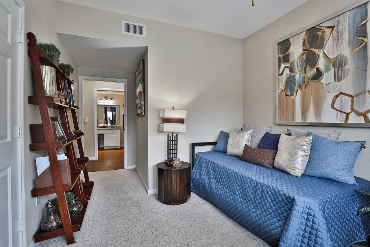Interior bedroom with a blue quilted daybed, side table, ladder shelf, and abstract art.