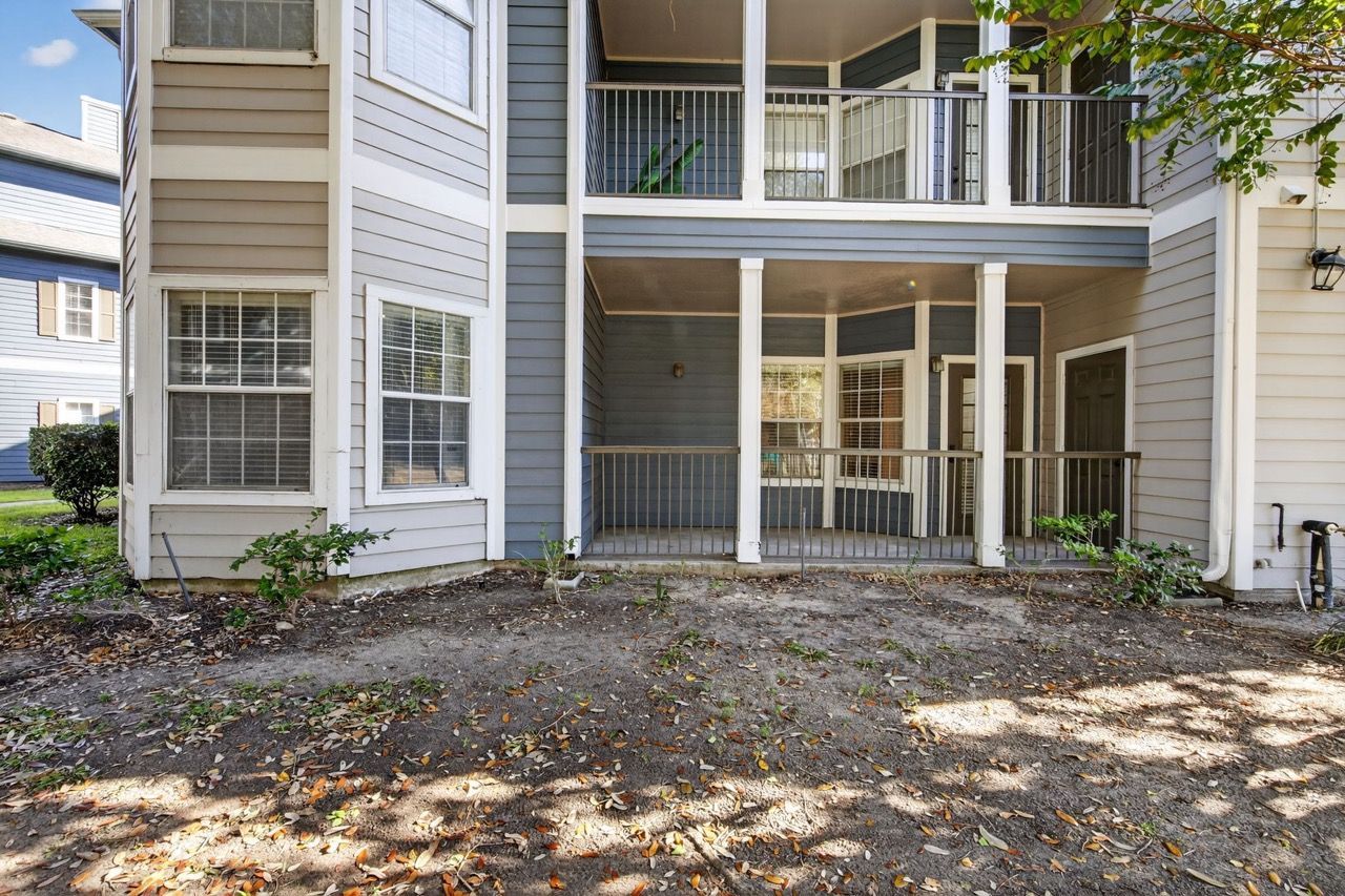 Ground-level porch area with white columns and railing in front of a multi-unit apartment building.