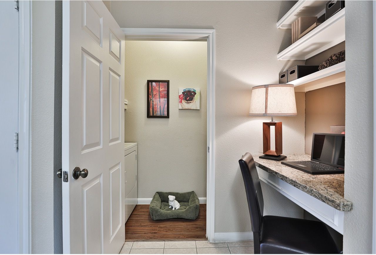 Apartment office area with granite desk, laptop, shelves, lamp; laundry closet with washer/dryer nearby; dog bed on floor.