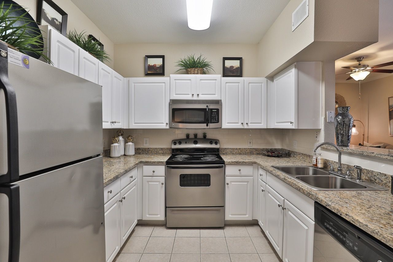 Bright kitchen with white cabinets, granite counters, stainless steel fridge, range, microwave, and double sink.