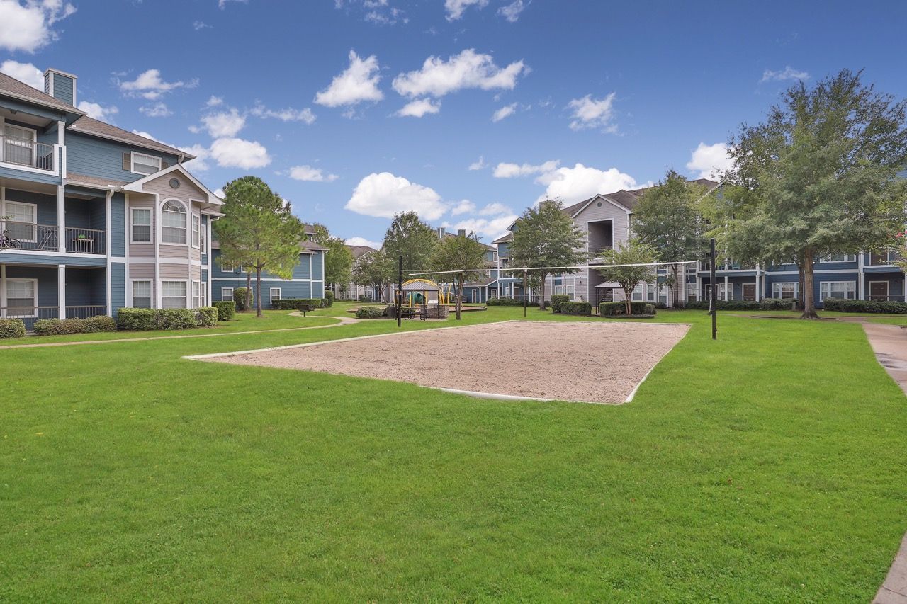 Exterior view of a multifamily property courtyard with a sandbox, playground, and green lawn.