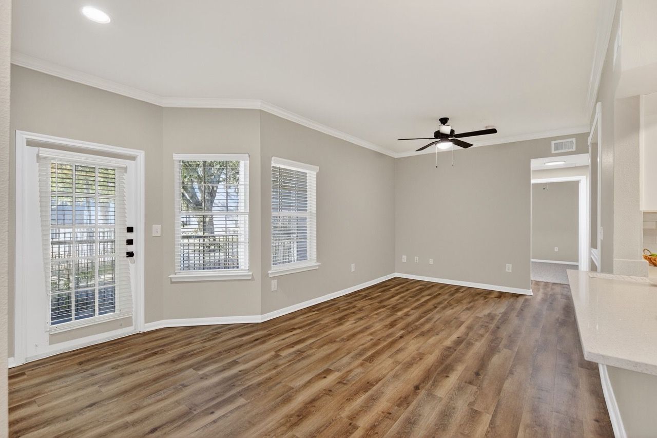 Bright living room with wood-like flooring, neutral walls, large windows, and a ceiling fan.