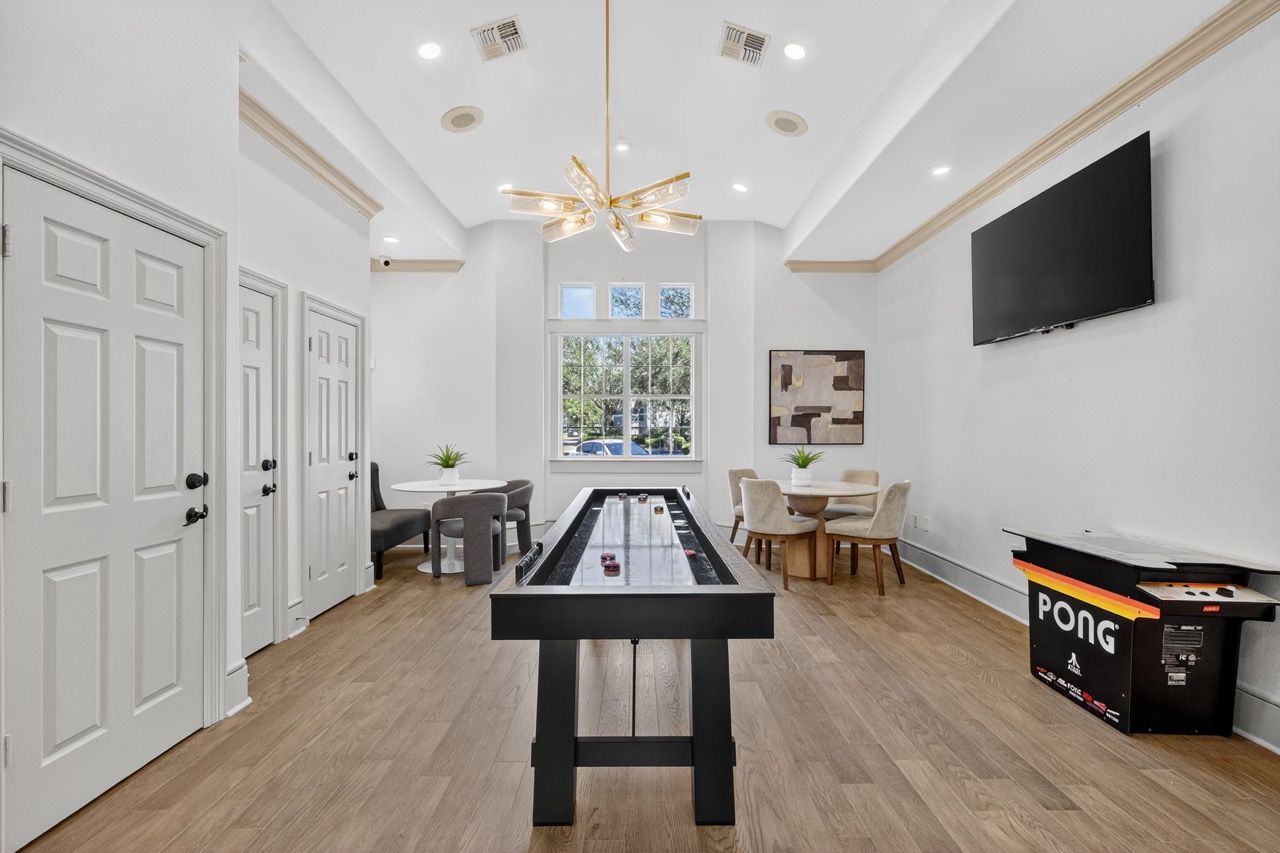 Bright community recreation room with foosball table, seating, and a wall TV.