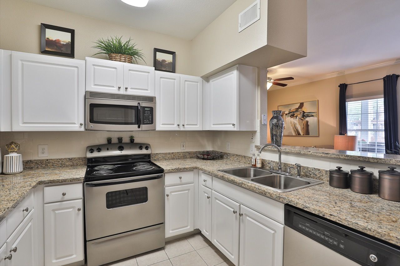 White kitchen with granite countertops, stainless steel stove and double sink.
