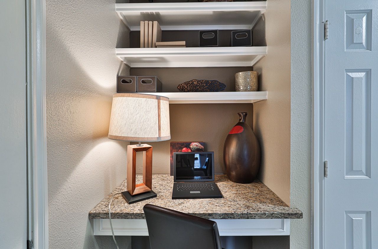 Compact built-in desk alcove with laptop, lamp, and organized shelves.