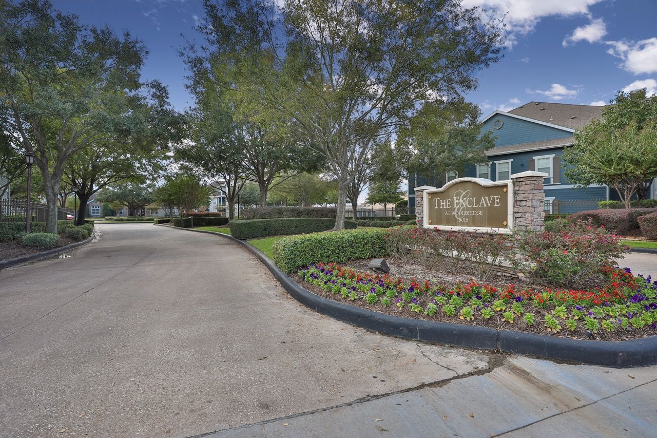 A paved entrance road leads to a stone sign for The Park at Laurel Oaks, surrounded by landscaping, trees, and sky.