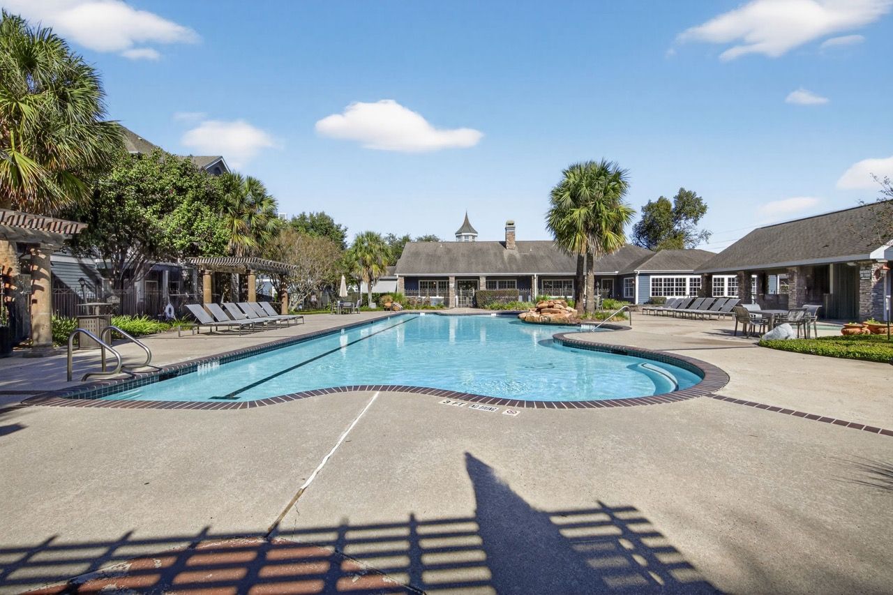 Outdoor pool at a multifamily community with lounge chairs and palm trees.