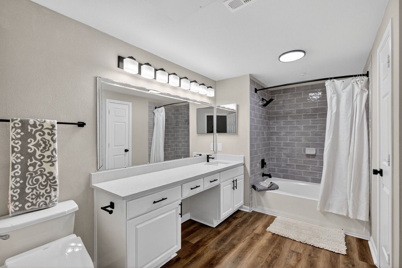 Bathroom with double-sink vanity, large mirror, shower/tub, and wood-look flooring.