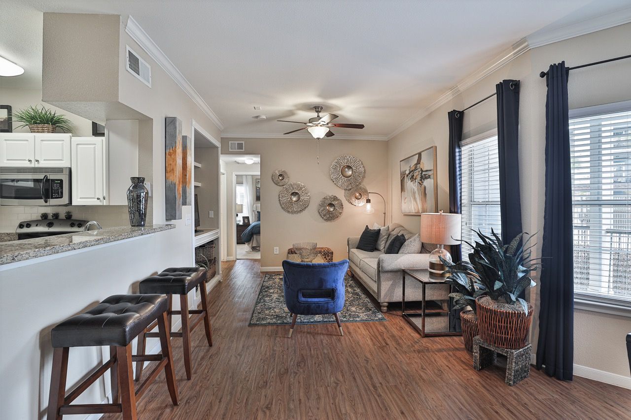 Open-concept living area with kitchen bar, couch, blue accent chair, and large windows with dark curtains.