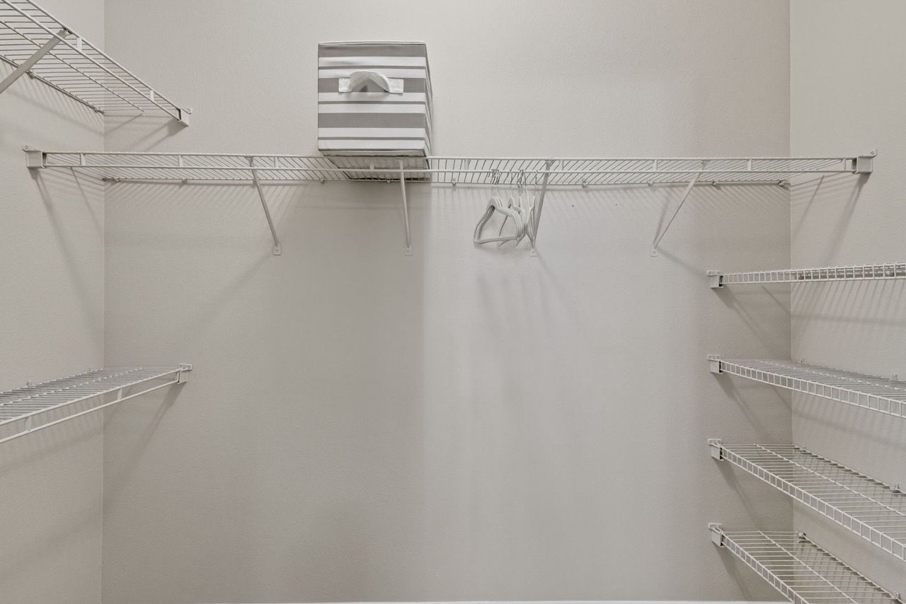 Empty walk-in closet with white wire shelving and a striped storage box on the top shelf.