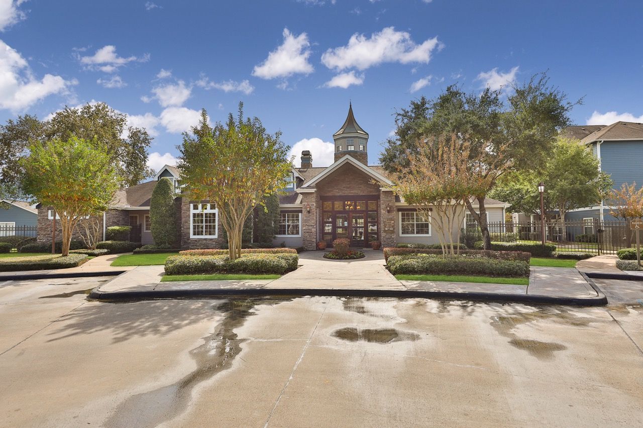 Exterior view of an apartment community building with a central entry and surrounding trees.