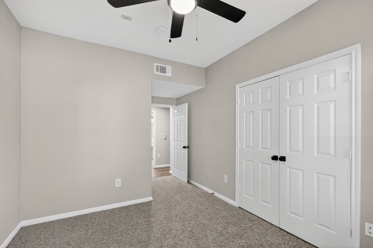 Interior bedroom with beige walls, carpet, a ceiling fan, and a double-door closet.