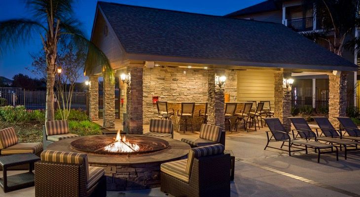 Outdoor communal lounge area at dusk with a fire pit, cushioned chairs, and a covered pavilion.