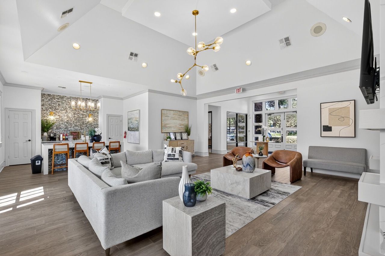 A spacious, modern apartment lounge with high ceilings, neutral furniture, a light-filled open floor plan, and hardwood.