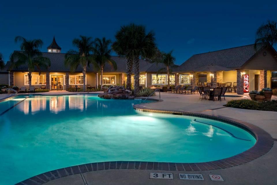 Night view of a resort-style pool with palm trees and a lit clubhouse.