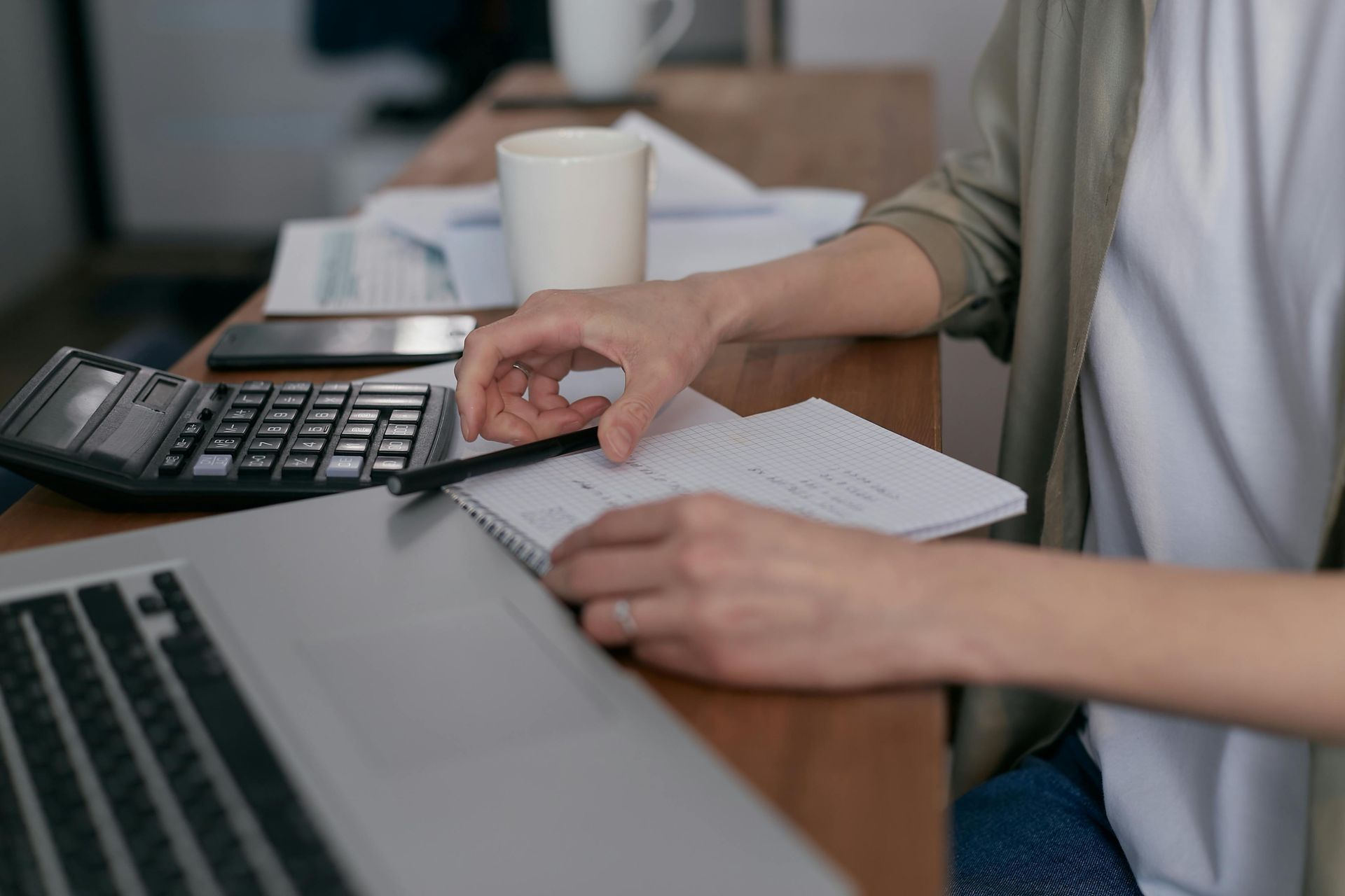 A woman is sitting at a table using a laptop and a calculator.