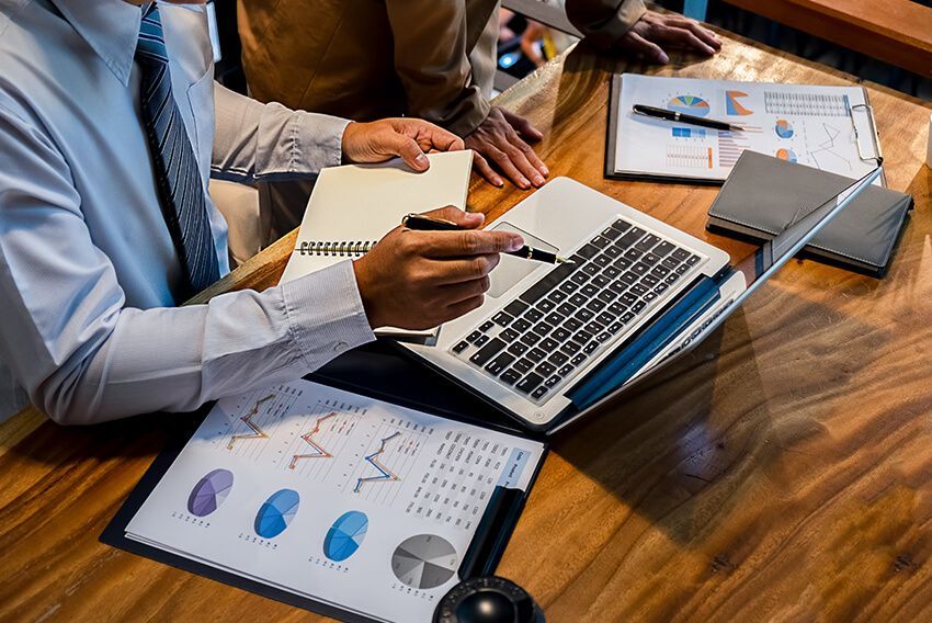 People reviewing financial charts and a laptop on a wooden table.