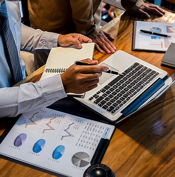 Businesspeople analyzing financial data with laptop, charts, and notebook at a table.