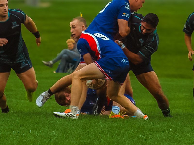 A group of rugby players are playing on a field and one player has the number 80 on his jersey