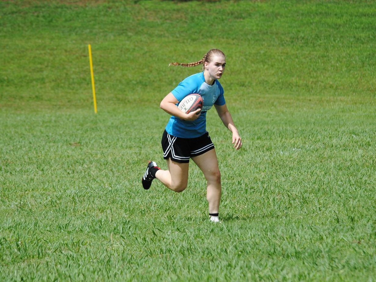 A woman is running with a rugby ball on a field.