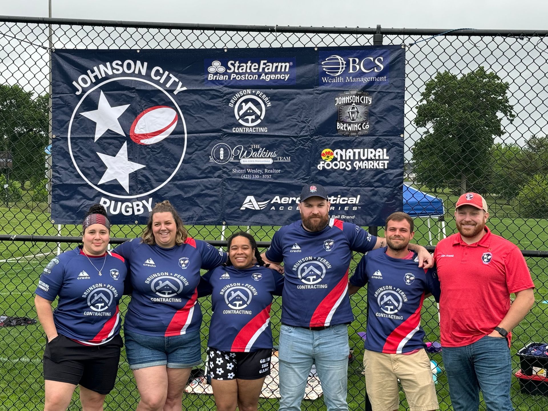 A group of people are posing for a picture in front of a johnson city rugby banner.