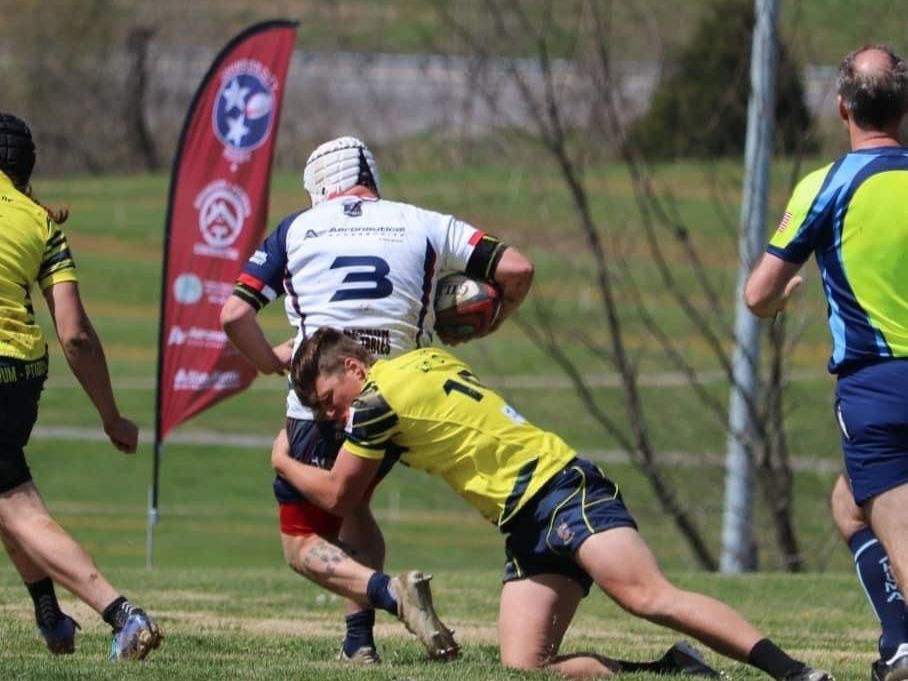 A rugby player with the number 3 on his jersey is being tackled by another player