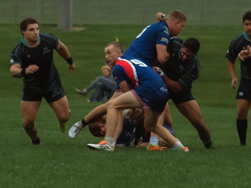 A group of rugby players are playing on a field and one player has the number 80 on his jersey