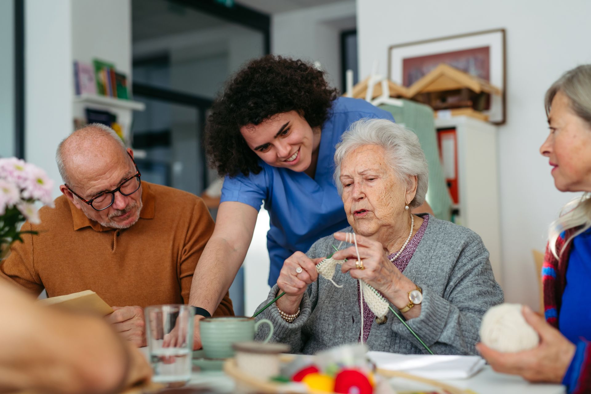 Caregiver assists elderly residents with crafts at a table, indoors. Caregiver assists elderly residents with crafts at a table, indoors.