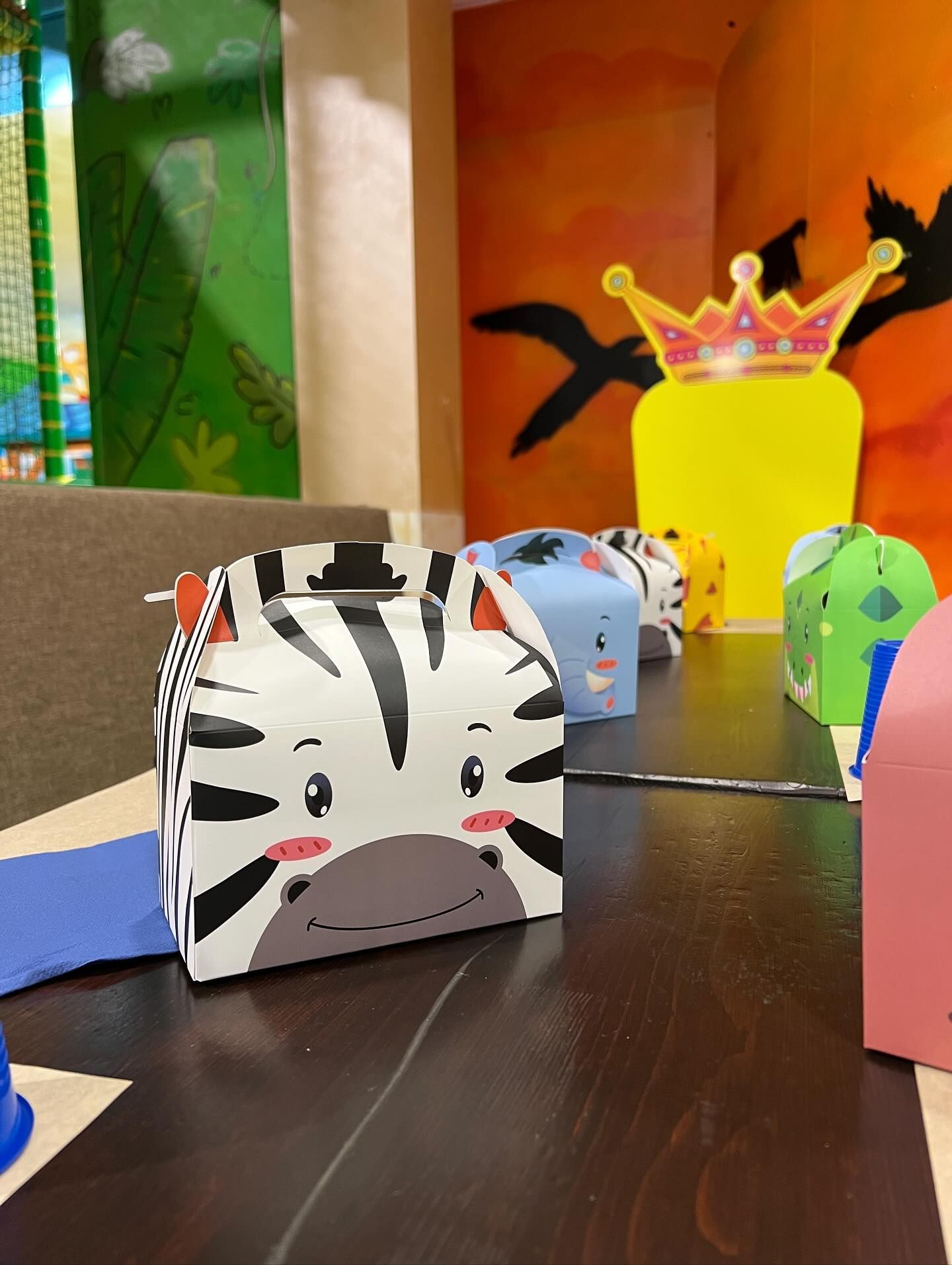 Scatole portaconfetti a tema animali su un tavolo, tra cui una zebra, accanto a un trono giallo ritagliato.