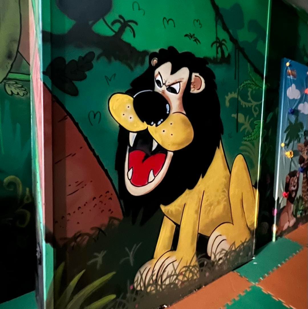 Leone dei cartoni animati con la bocca aperta e l'espressione arrabbiata su un murale della giungla.