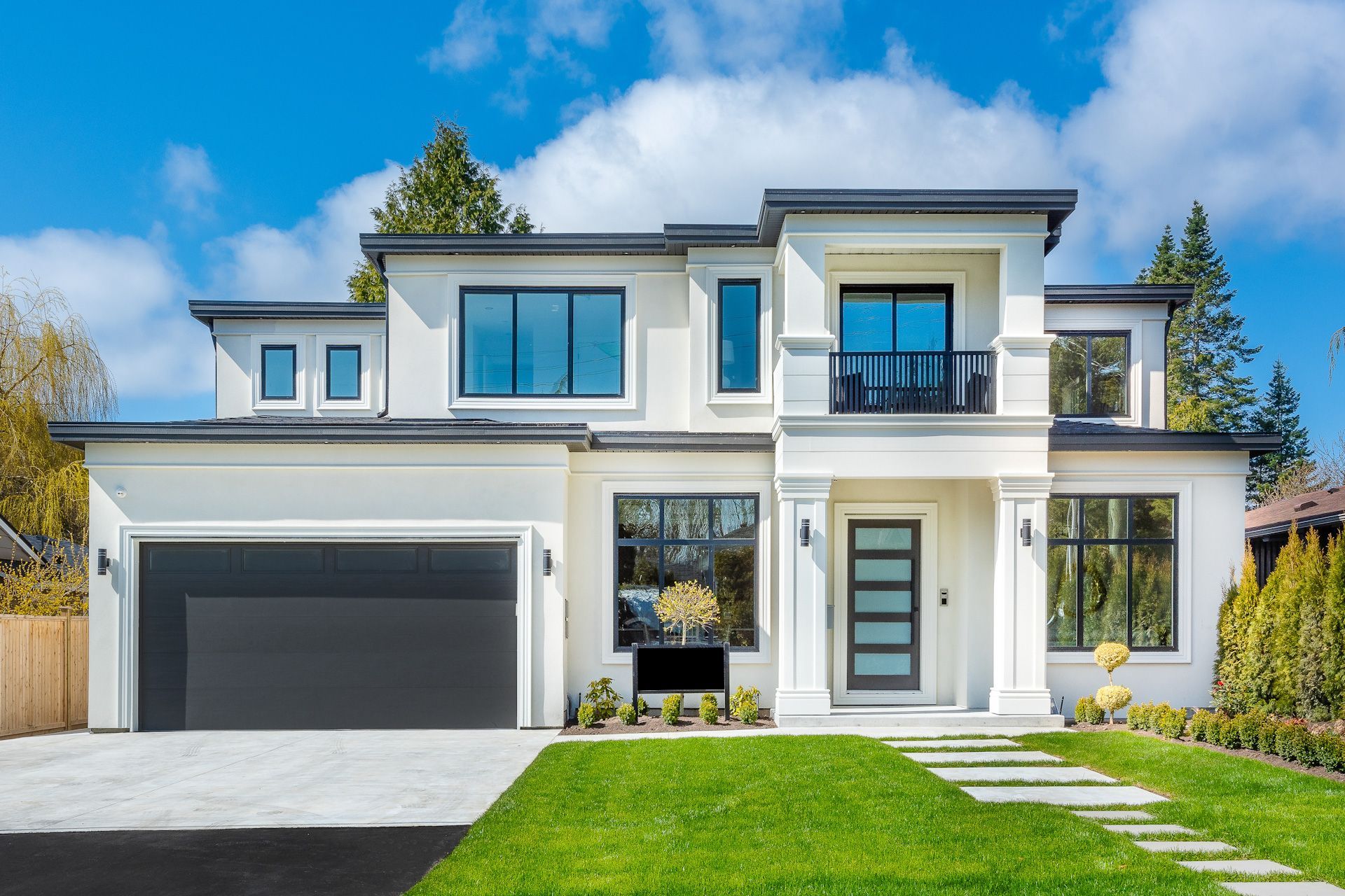 A large white house with a black garage door and a lush green lawn.