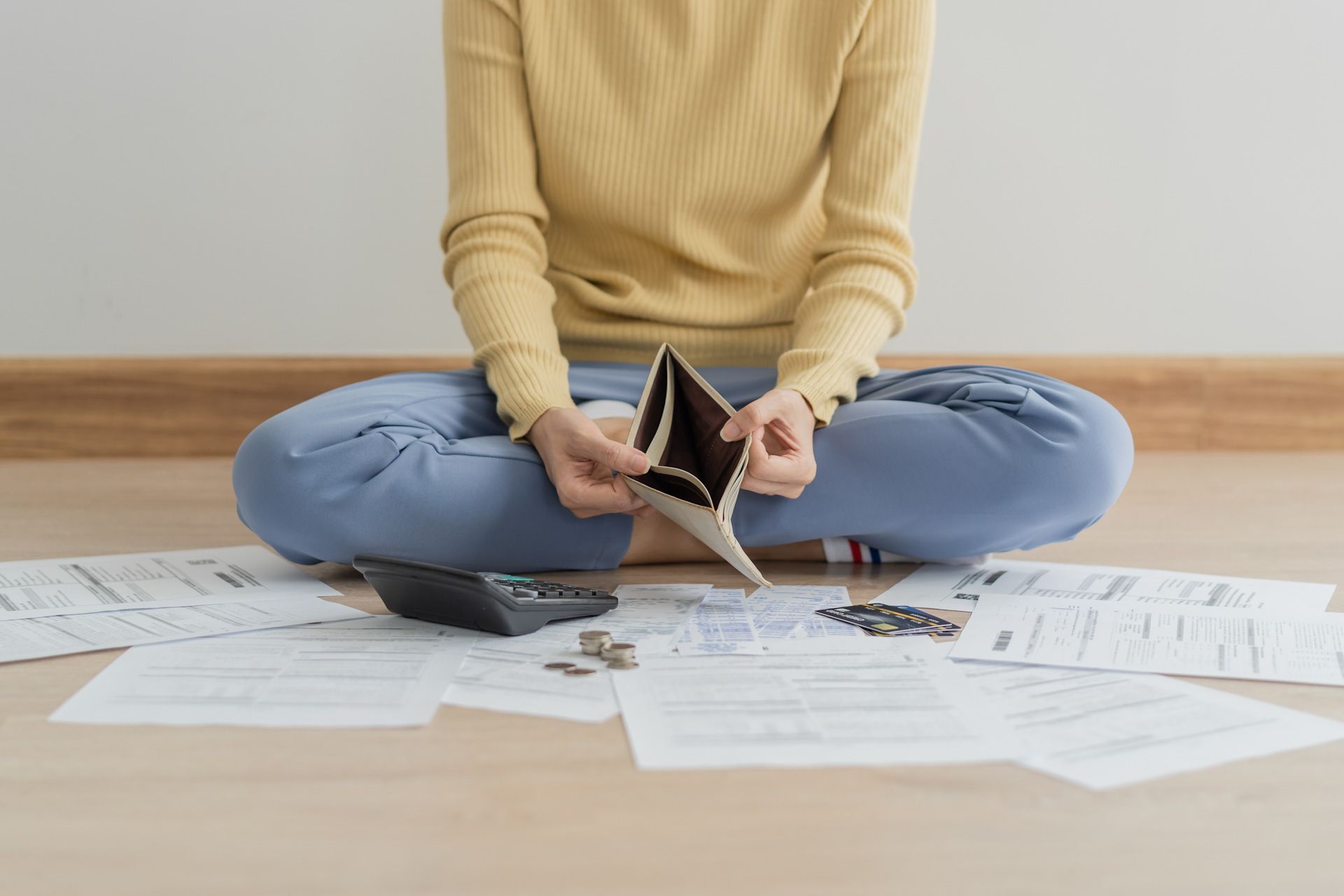 A woman is sitting on the floor holding an empty wallet and a calculator.