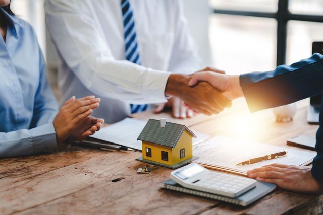 A group of people are shaking hands over a table with a model house on it.