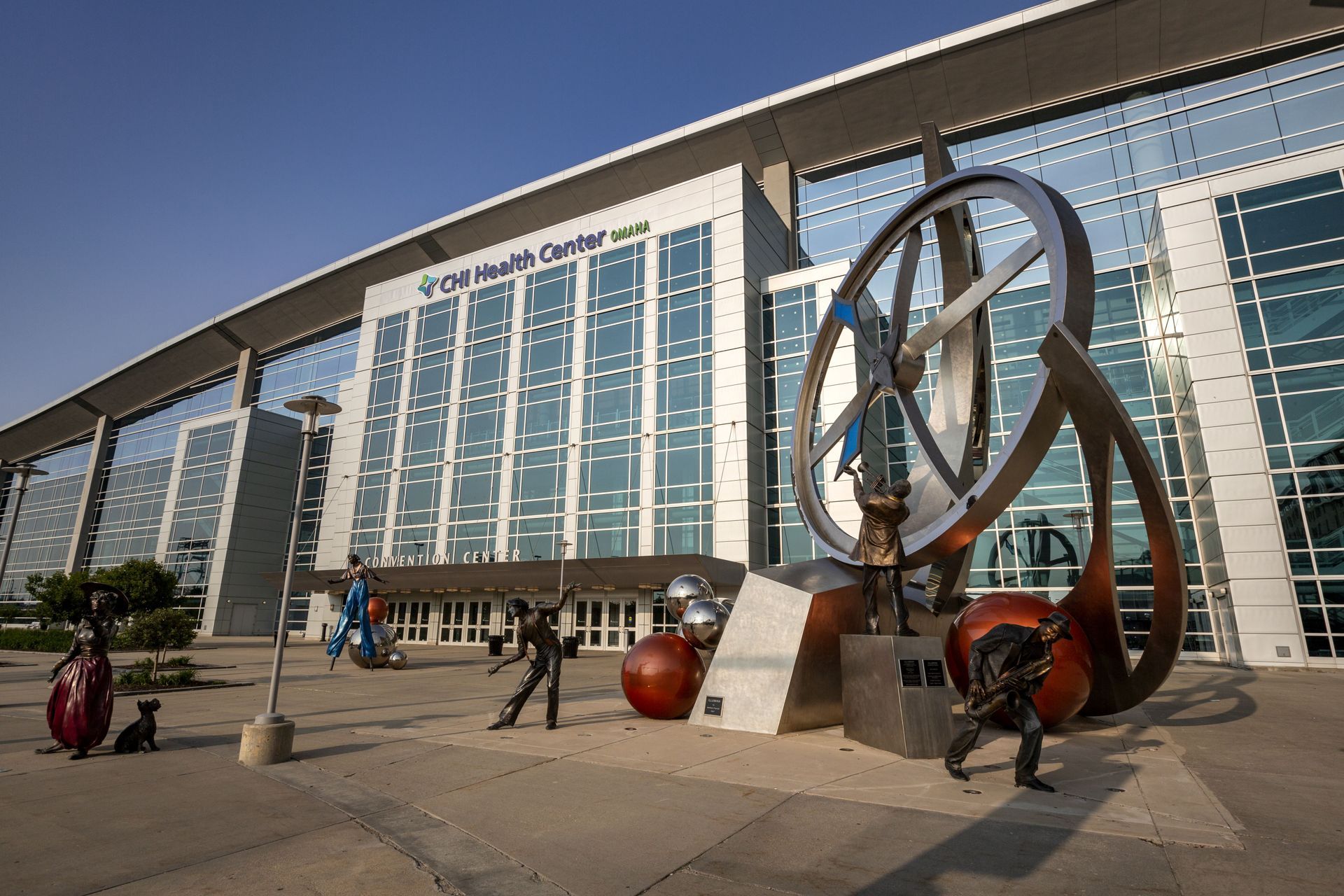 Modern building with glass facade, sculpture in front; sunny day.
