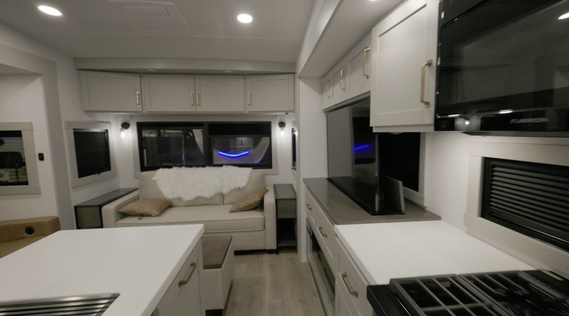 Interior view of a modern RV, showing kitchen area with stove and microwave, and a living area with a couch.