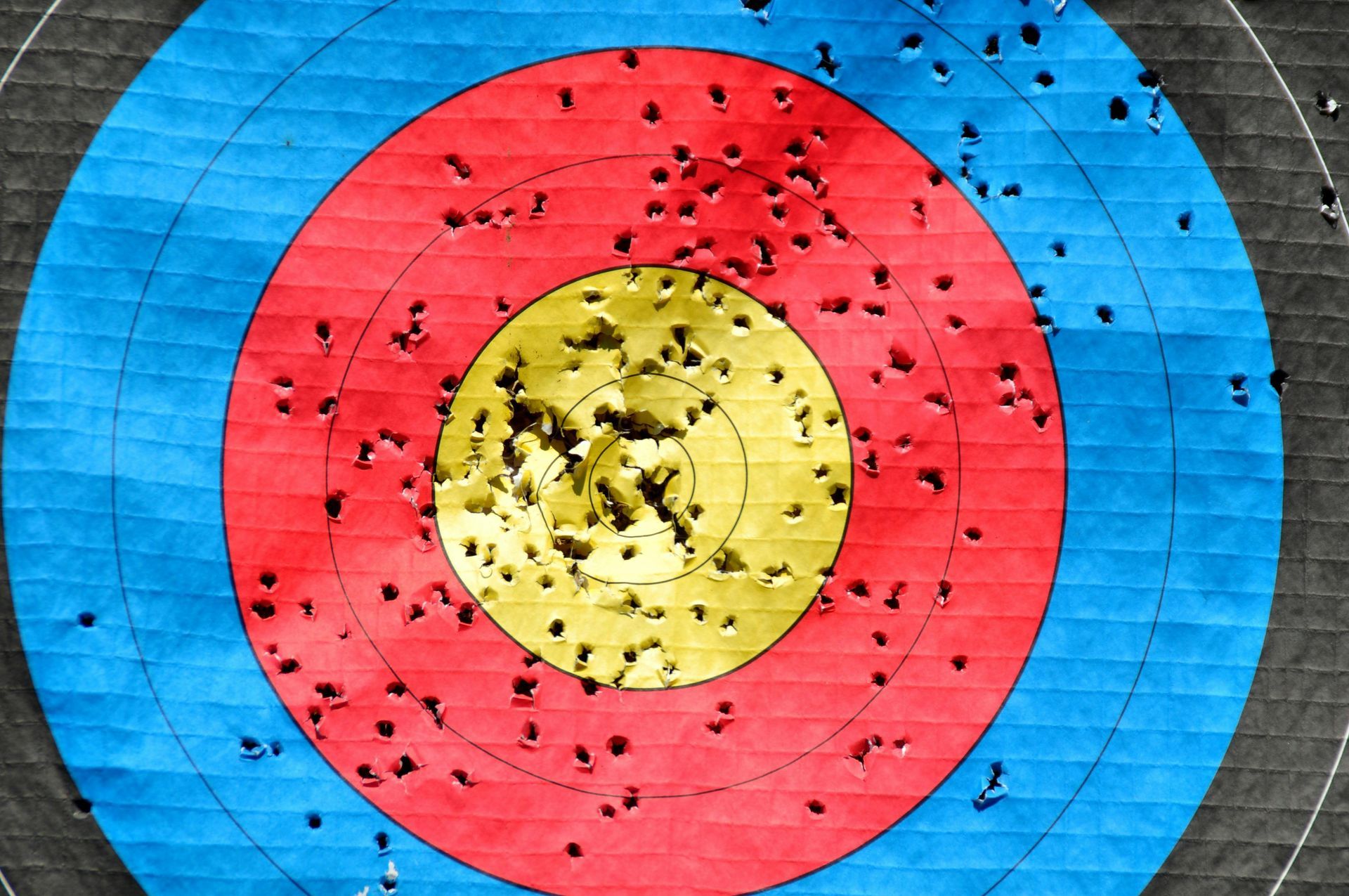 Archery target with numerous arrow holes, concentrated near center. Red, yellow, and blue rings.