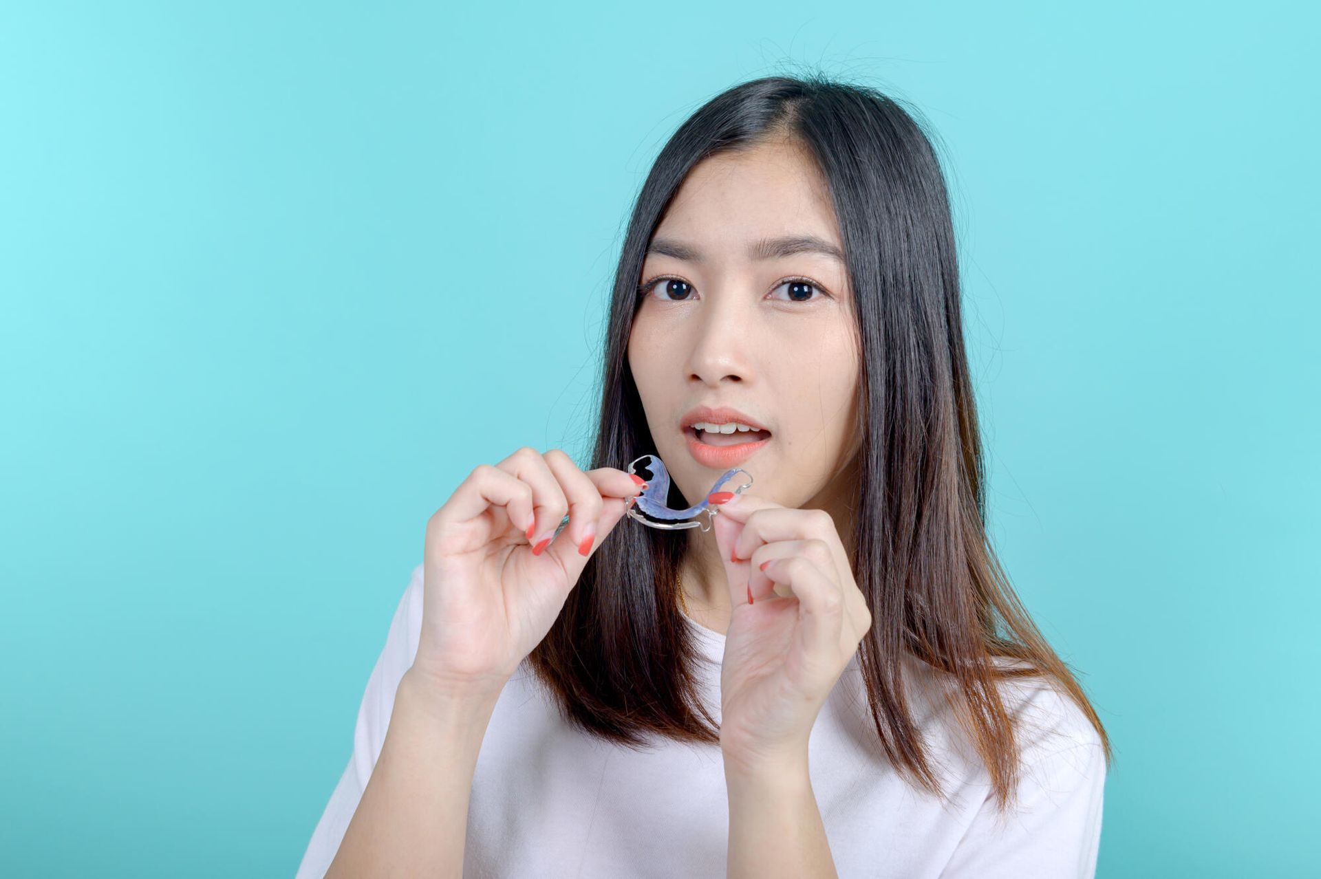 Woman holding clear dental retainer, light blue background.