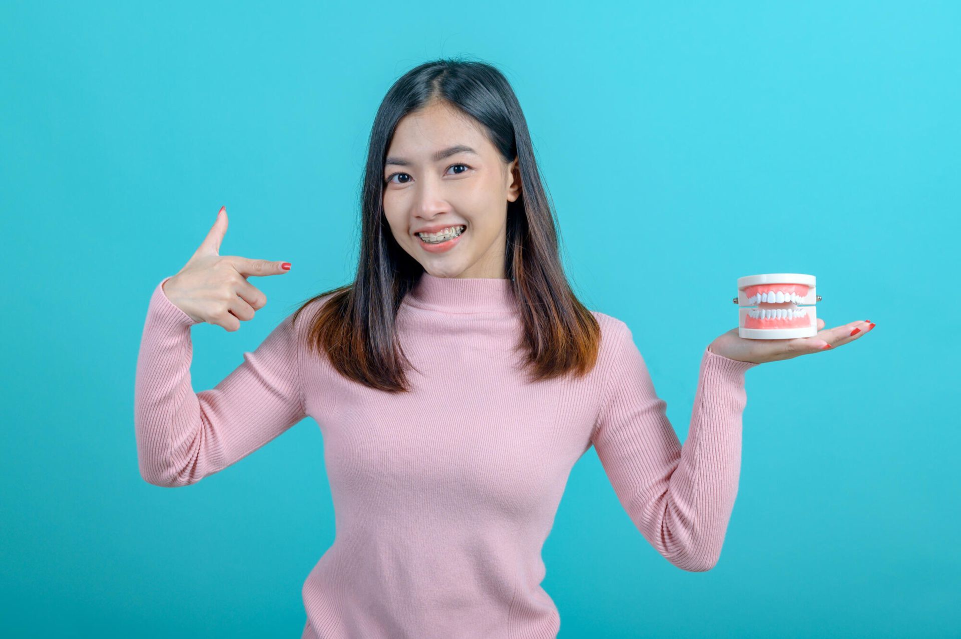 A woman is holding a model of teeth in her hand and pointing at it.