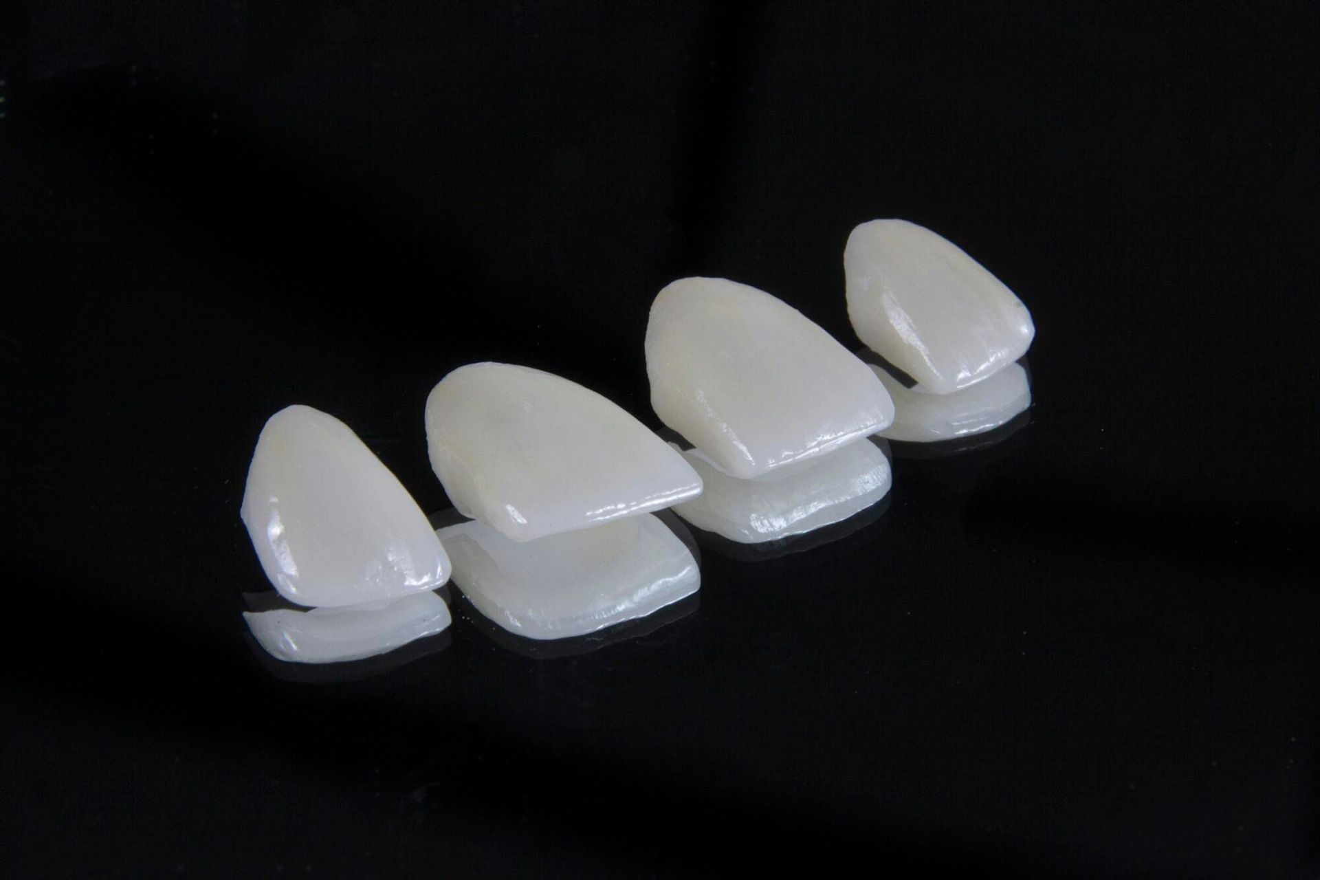 Four porcelain dental veneers on a reflective black surface.