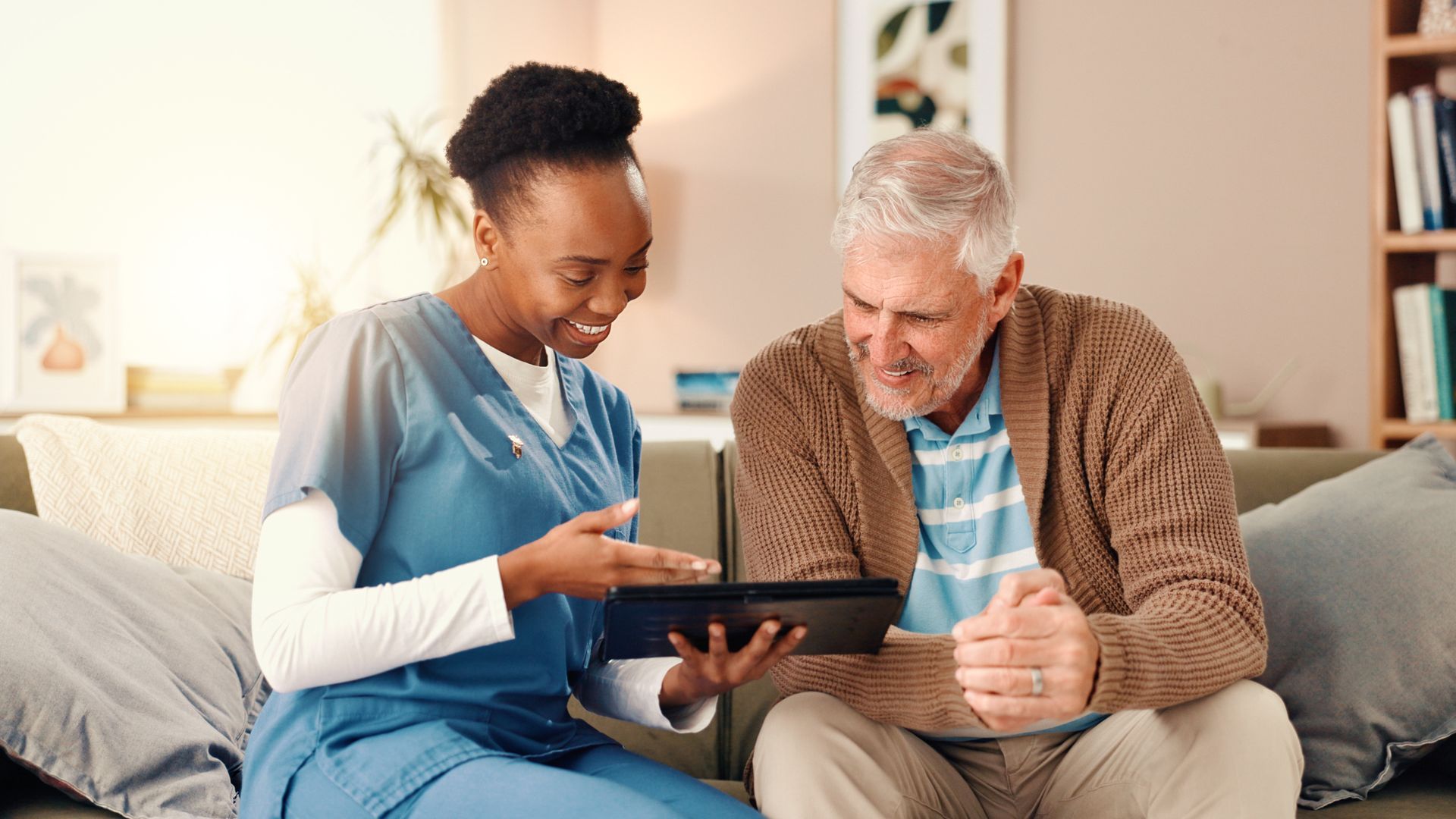 Nurse showing tablet to senior in a living room, both smiling.